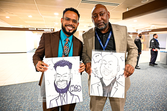 2025 Federal Airport Employee Appreciation Day of two men standing side by side, while holding caricature drawings of themselves.