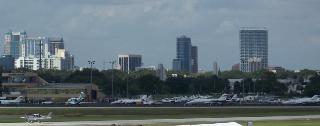 Outside view of Orlando Executive Airport with airplanes parked. Downtown Orlando is behind in the distance.