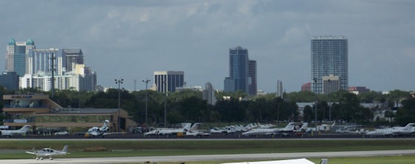 Outside view of Orlando Executive Airport with airplanes parked. Downtown Orlando is behind in the distance.