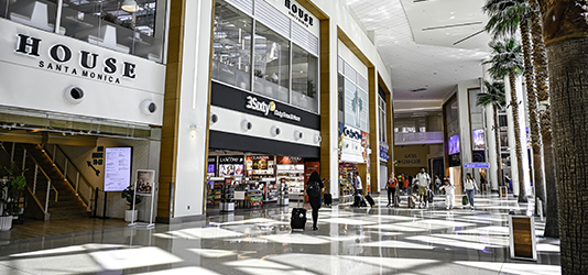 People walking down Terminal C hallway with concession stores on the left and Palm Court on the right