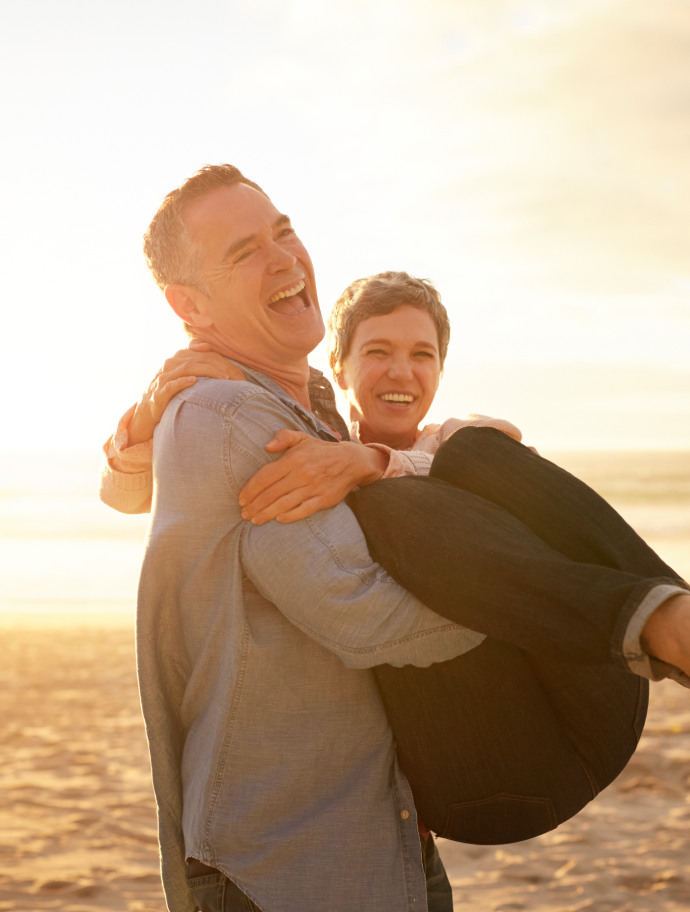 A laughing man carrying his smiling wife on the beach