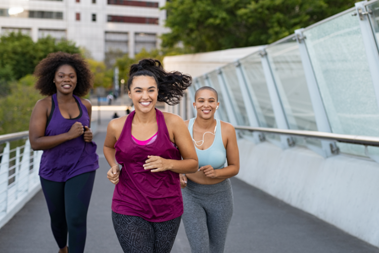 Three women wearing active wear running on a bridge