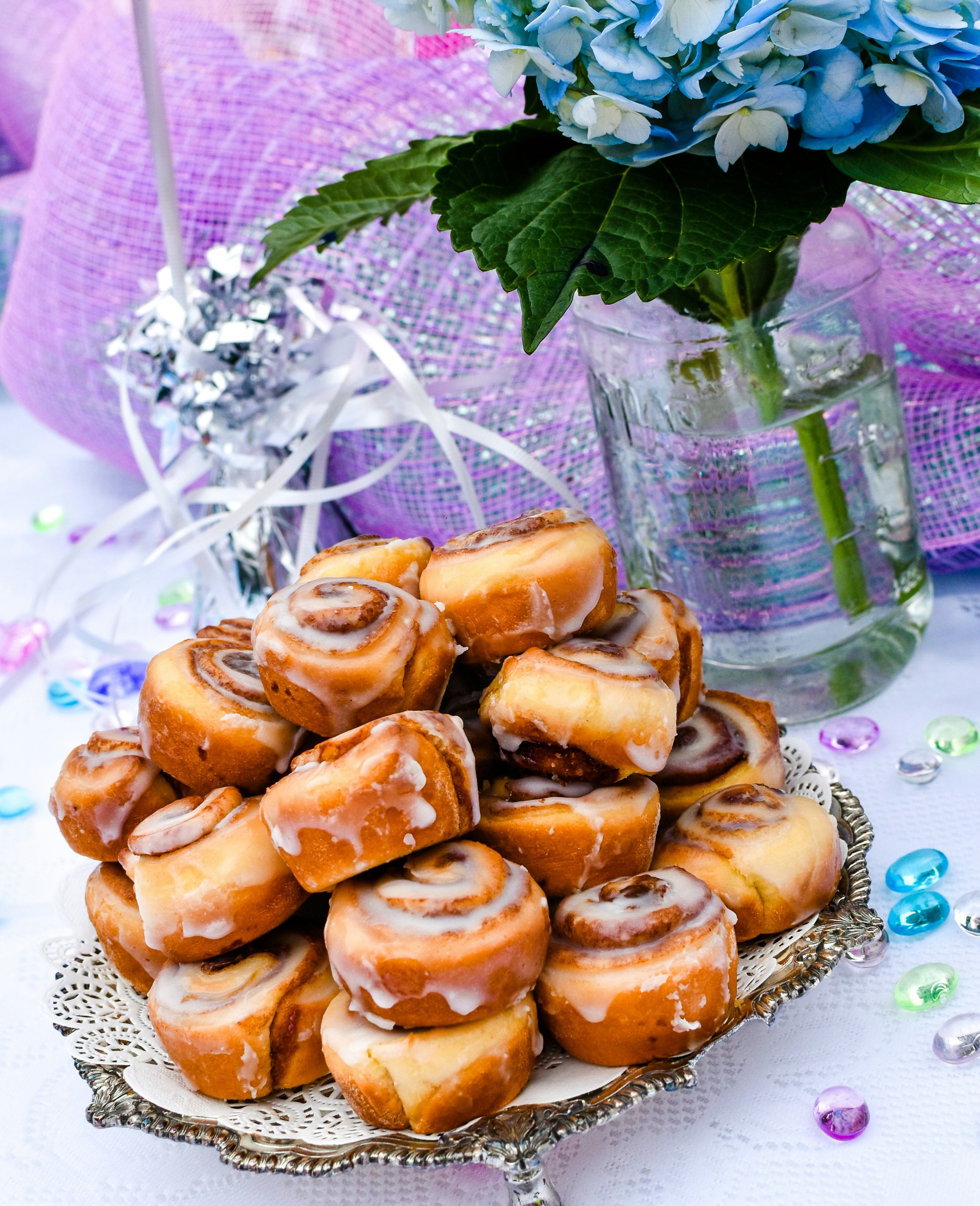a big pile of cinnamon rolls on a table arranged with flowers and jewels