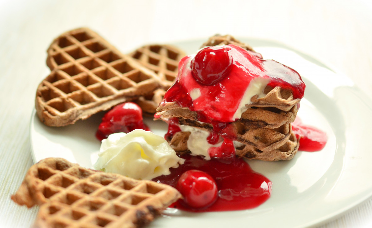 a plate of heart shaped waffles in a stack with cream, sauce, and cherries