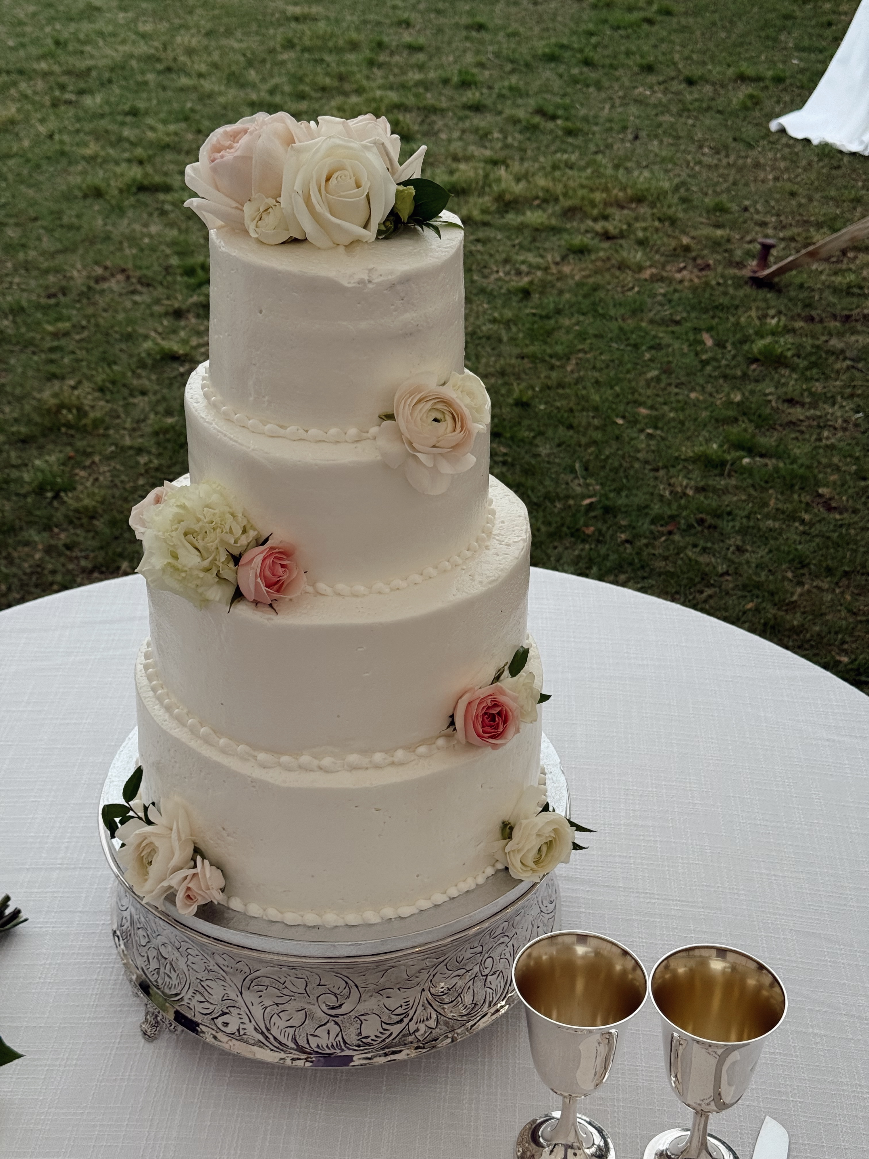 a white, four tiered wedding cake with decorative roses