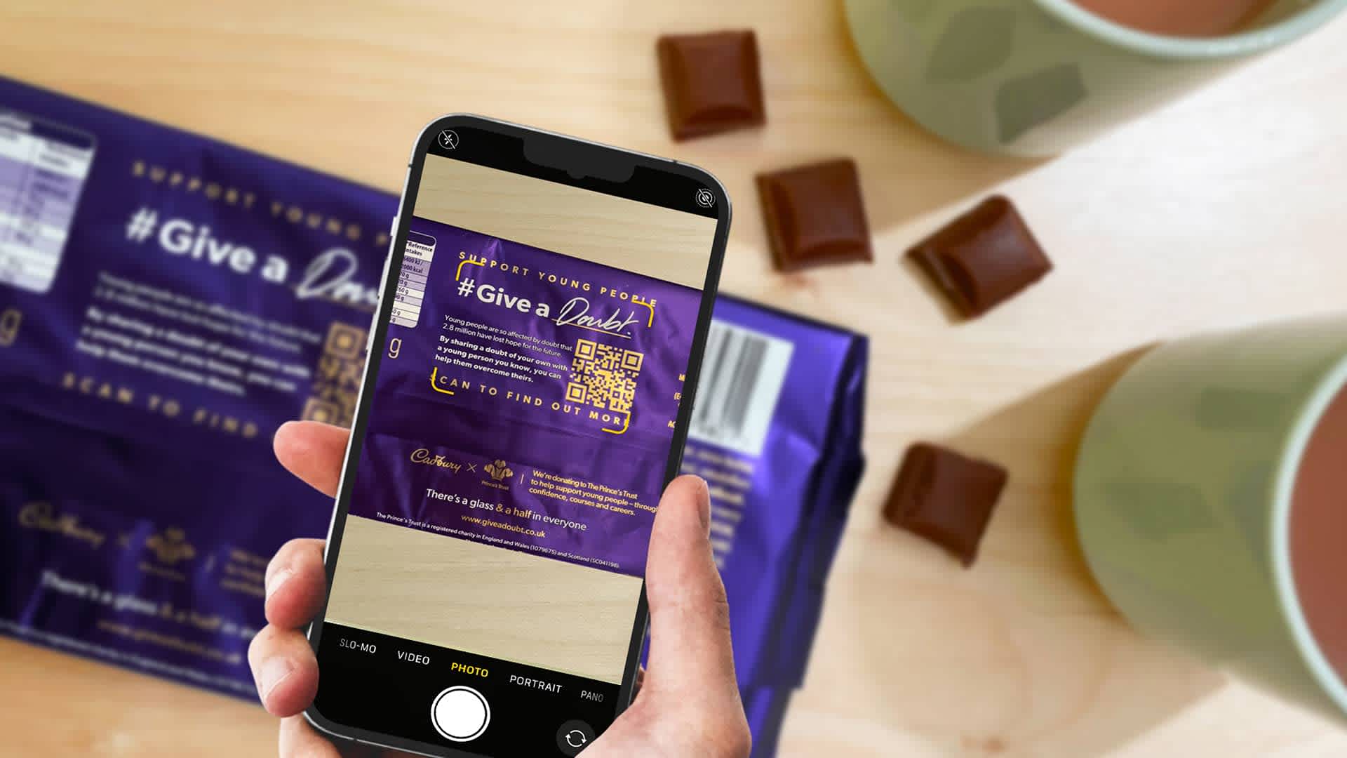 Photo of a smartphone displaying a camera app with a QR code featuring Cadbury packaging and the hashtag #Give a Doubt.