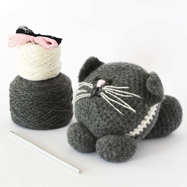 two balls of yarn in grey and white next to a crochet hook and a grey crocheted cat