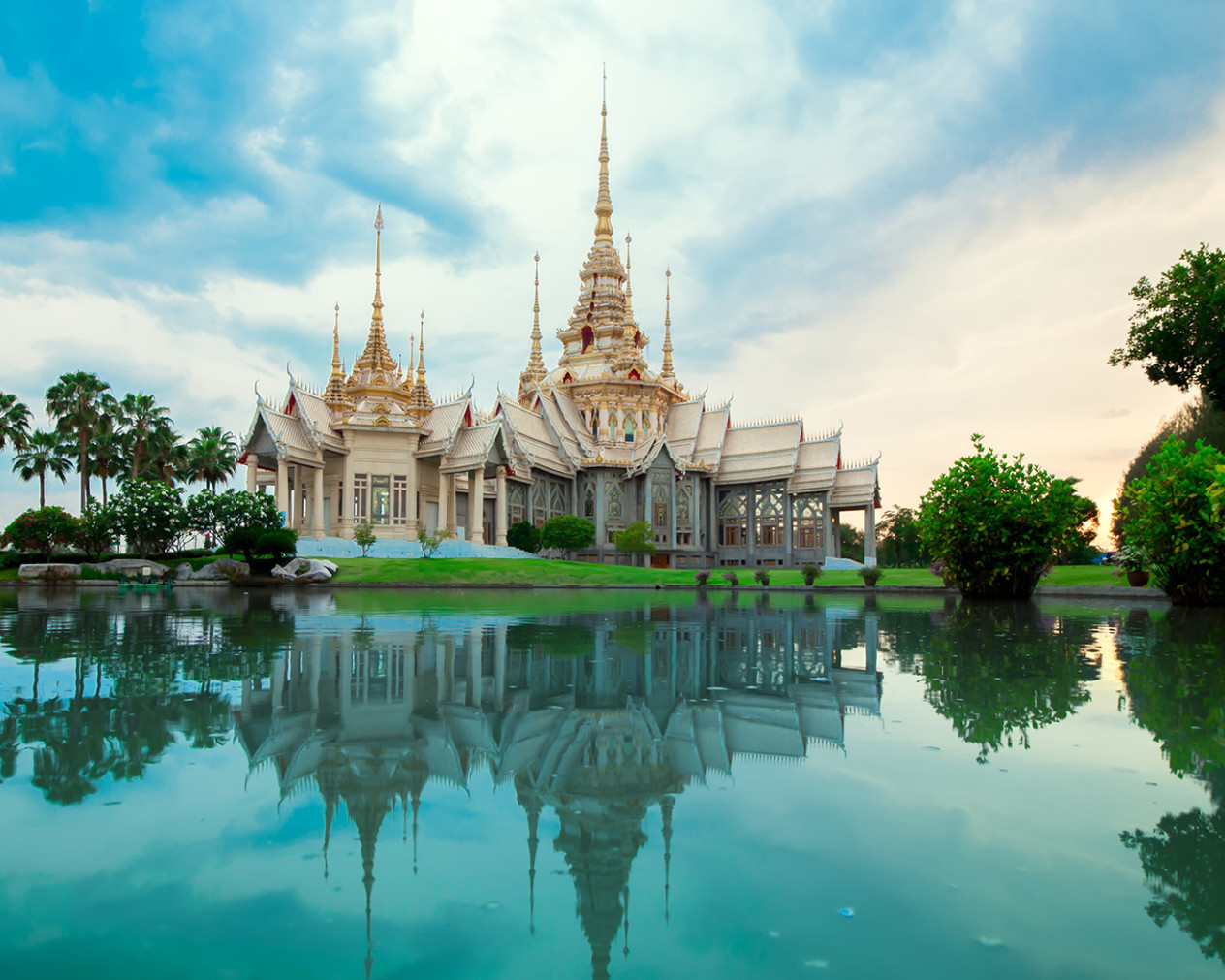 gold and white spired temple overlooking blue water in thailand