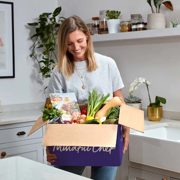 woman in white t-shire holding a purple Mindful Chef Recipe Box filled with vegetables