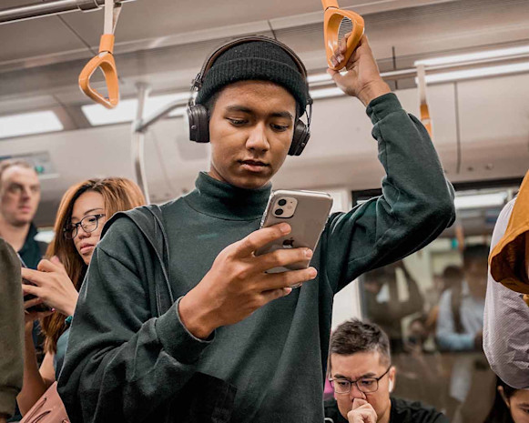 person wearing a green sweatshirt and headphones on a subway train holding a smartphone