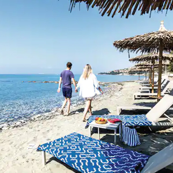 couple walking along beach with sun loungers and palm umbrellas