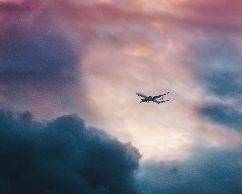 plane flying in a pink, purple and blue sky with clouds