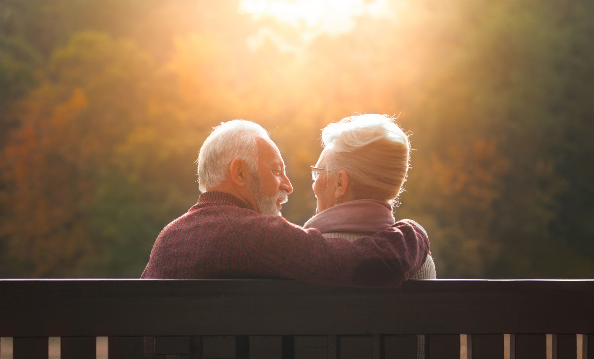 A man and woman sitting on a bench at sunset