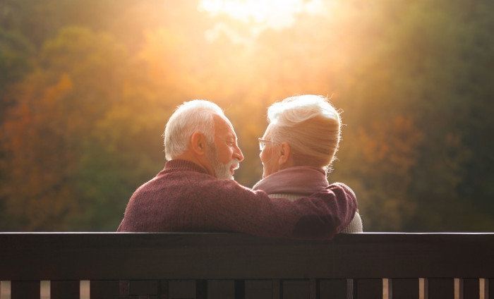 A man and woman sitting on a bench at sunset