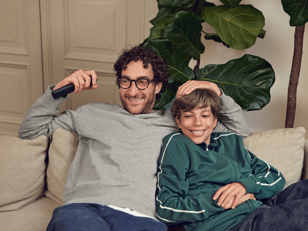 En smilende far og søn sidder i en sofa og ser tv