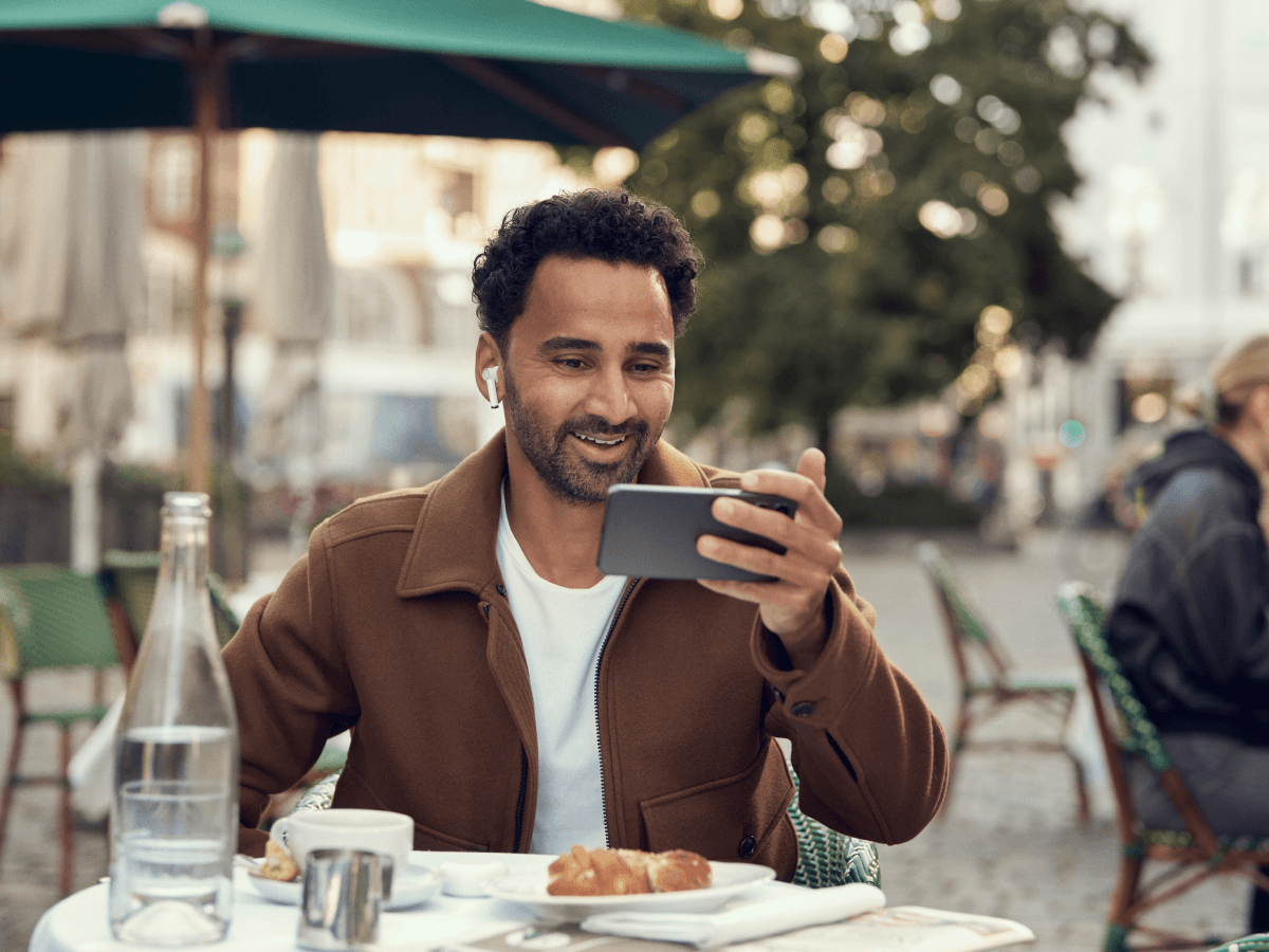 En mand med hvide airpods sidder på en café og ser på sin mobiltelefon