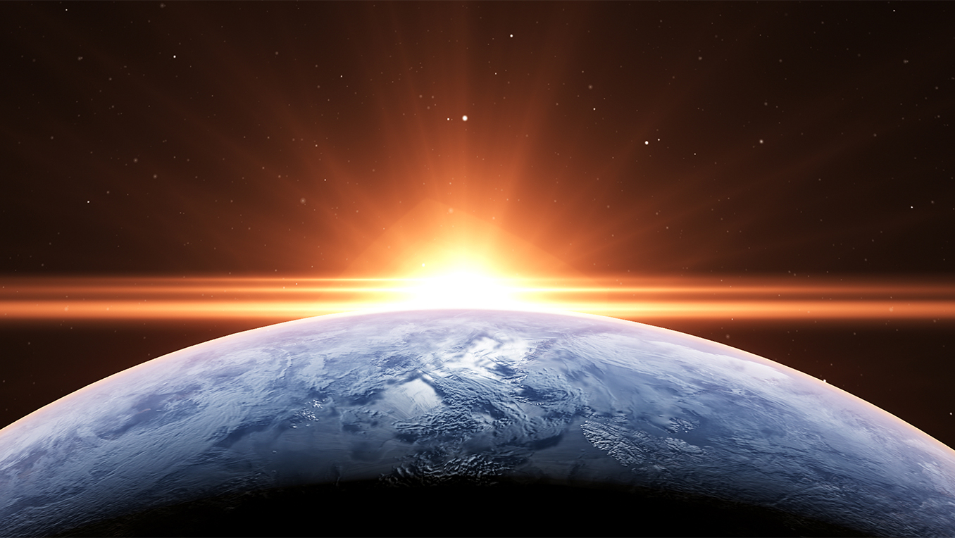 Wide angle image of the sun rising over the earth in space casting a bright horizon
