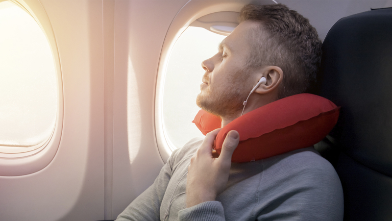 Traveler sits happily on a plane and listens to audiobooks on his headphones with sun glaring through the airplane window