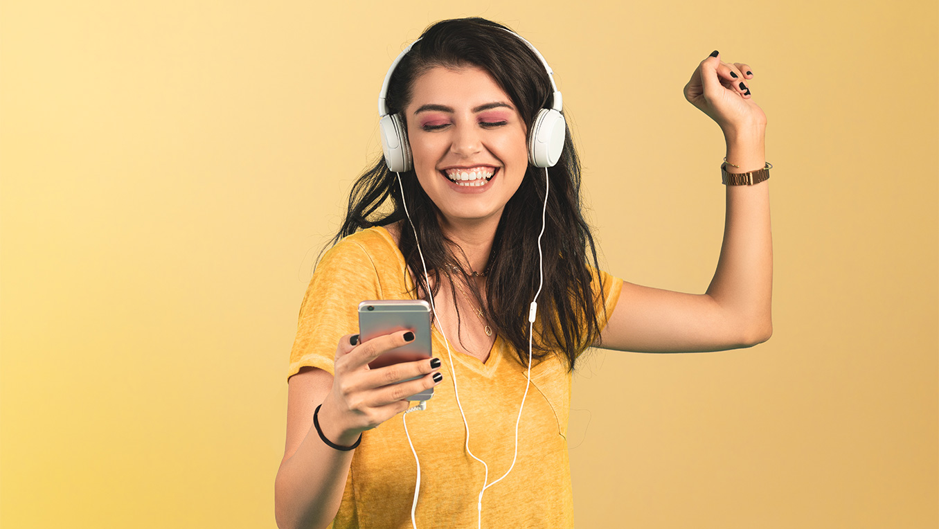 A girl in a yellow t-shirt listens happily to an audiobook while smiling and fist pumping in the air