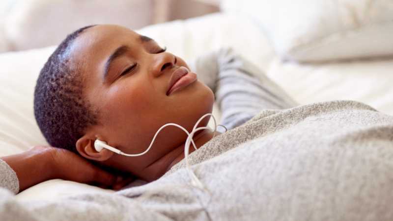 A woman lies in bed happily listening to audio content with earbuds
