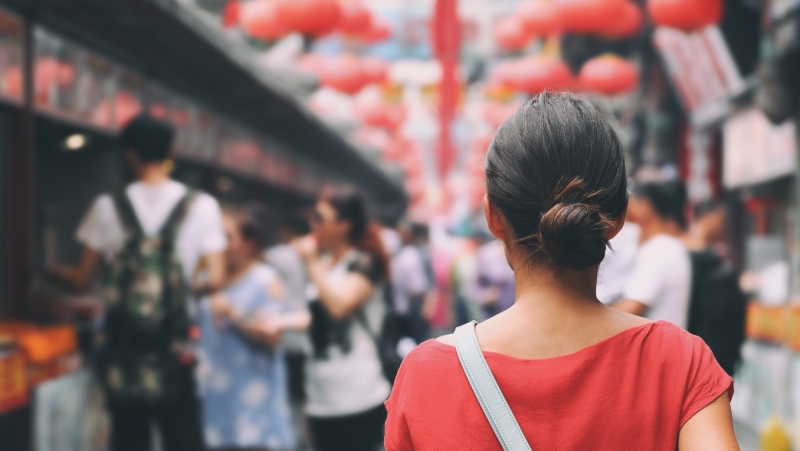 A photograph of a woman walking toward a busy Japanese marketplace