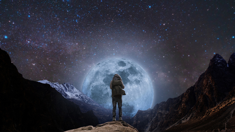 A solitary figure stands atop a mountain ridge, silhouetted by a large, full moon in the background