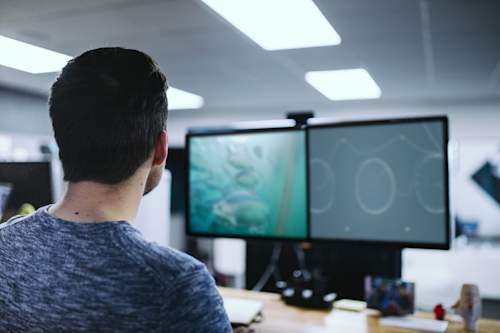 En person ser på live videostrømming fra en blueye undervannsdrone på pc skjermene ved pulten sin