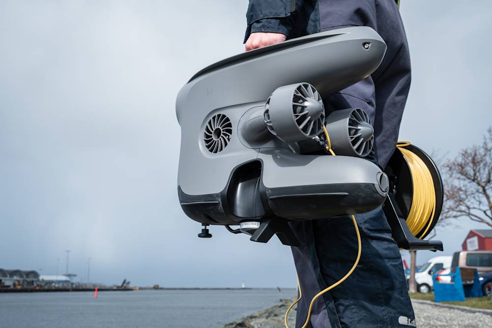 Person holding X3 with DVL and tether reel by the river