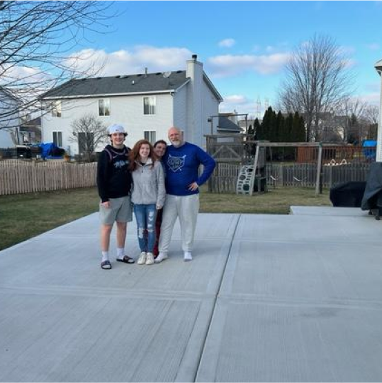 Family with husband, wife, teenage boy & girl in a backyard with a swingset