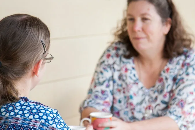 Girl speaking to woman at table