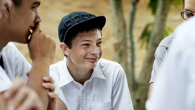 A younger teenager sitting and smiling with his peers