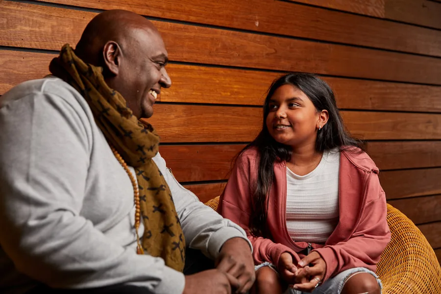 Image of a dad and his daughter sitting together outside. They are both smiling.