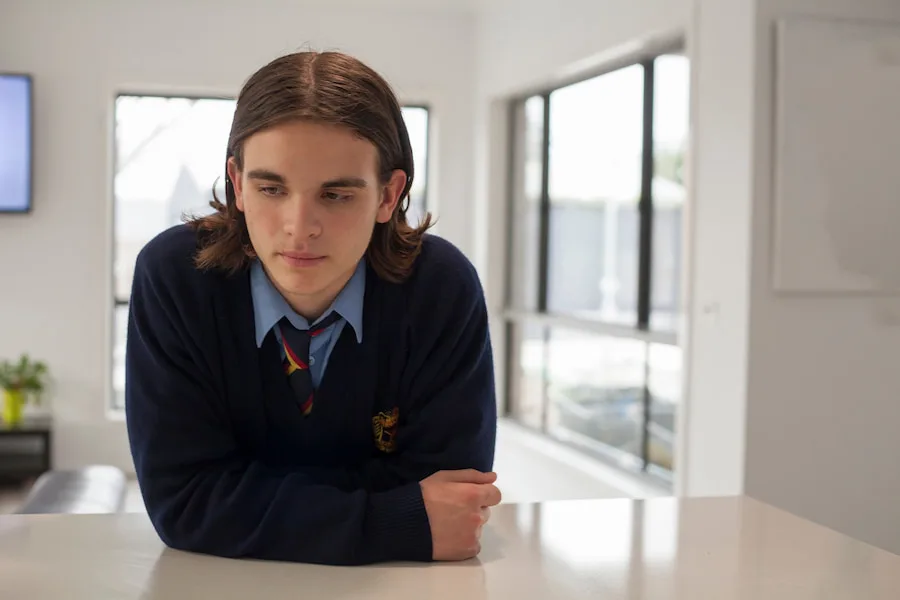 Image of a teenage boy standing at a kitchen counter, looking sad.