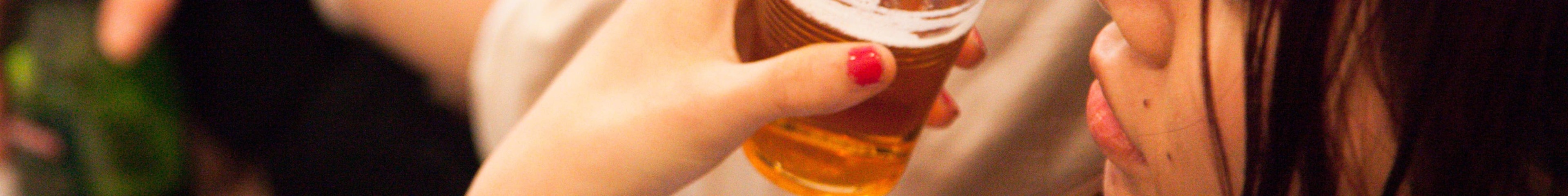 Image of a teenage girl holding a clear plastic cup filled with beer.