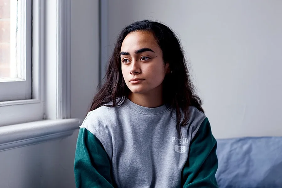 girl sitting on bed looking out window