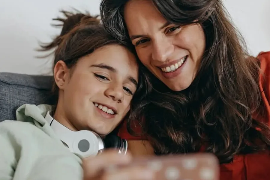 A mother and child sitting together and smiling at something they're watching on a phone.