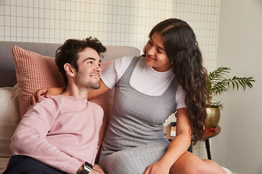 Image of two teens sitting together and smiling at each other on a bed.