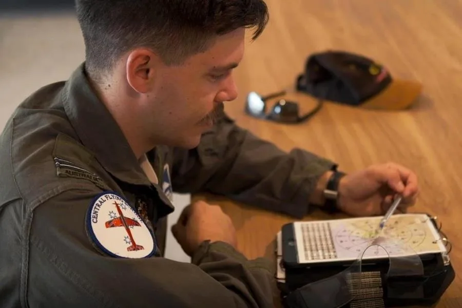 man in pilots uniform sitting at desk looking at map