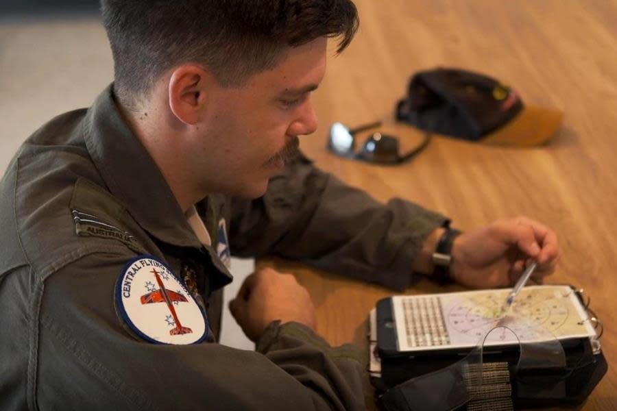 man in pilots uniform sitting at desk looking at map
