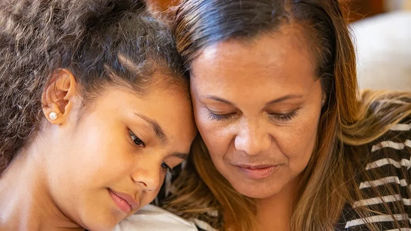 teenage girl sitting with mother resting forehead on mothers cheek