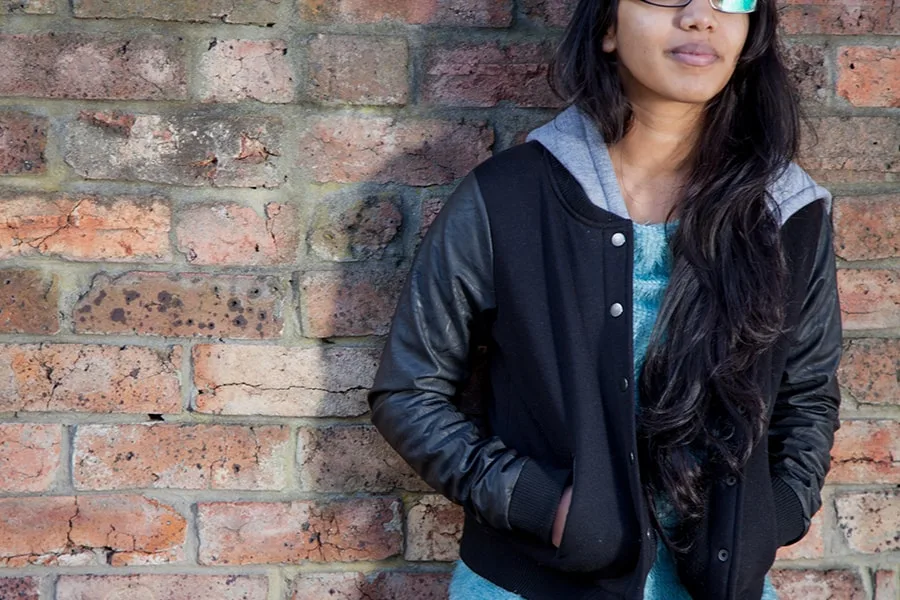 Half headless shot of girl leaning against brick wall with hands in pockets