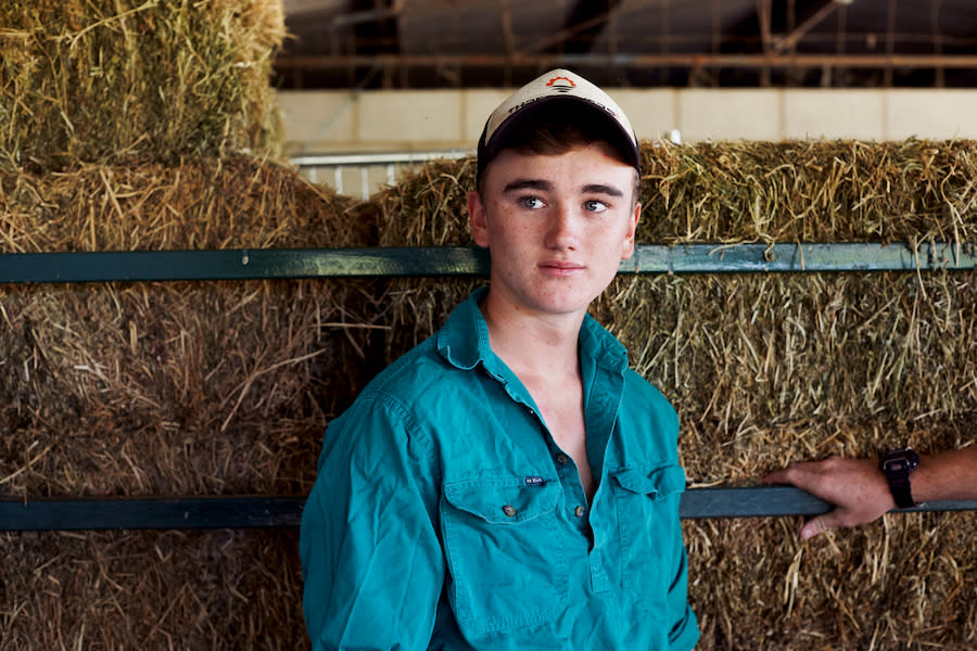 Image of a teen boy standing in front of some hay bales. He is looking away from the camera and isn't smiling.