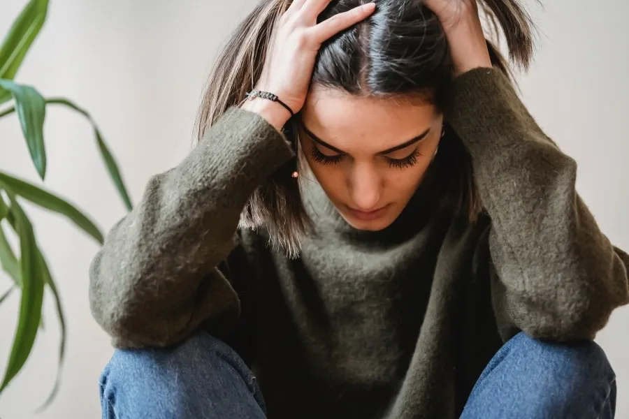 Young girl with dark hair and green jumper looking stressed, holding her head in her hands.