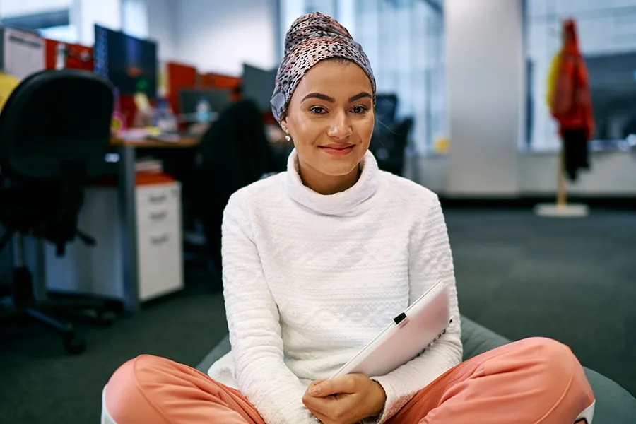 Angel girl sitting on beanbag smiling holding notebook with office in background