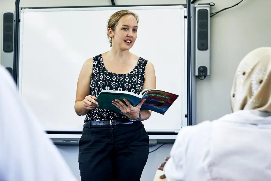 Teacher holding textbook talking to class