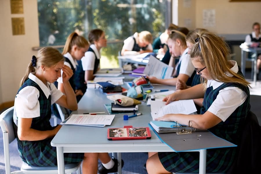 Students sit at table with workbooks concentrating