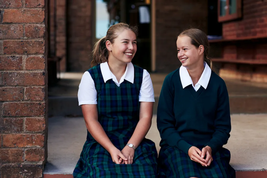 Two female students sitting on a step smiling at each other