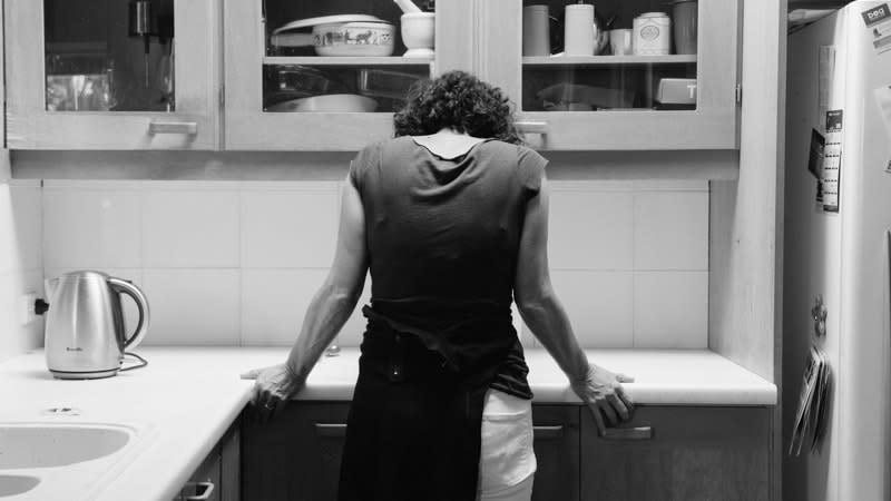 A mother standing at a kitchen bench hunched