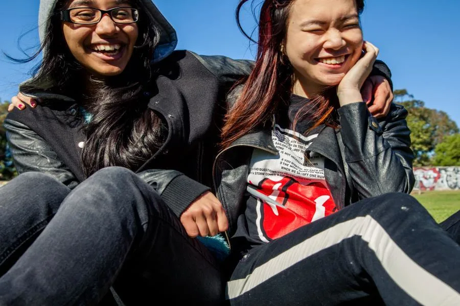 two girls laughing in park with arms around each other