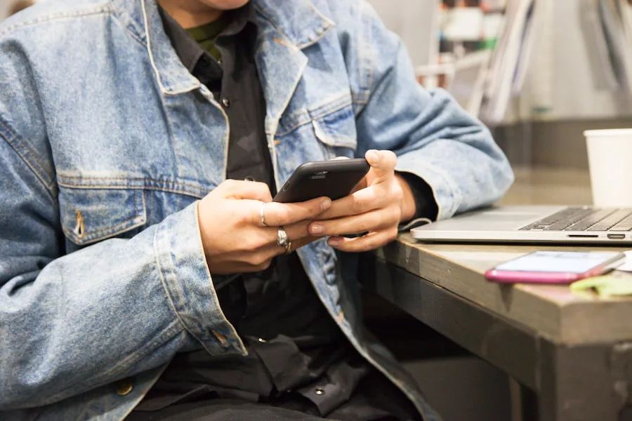 Image of a teen holding a phone, sitting on a desk next to a laptop.